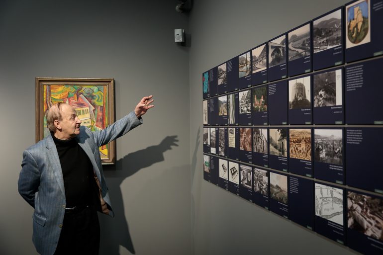 Karl A. Kubinzky führt durch die Ausstellung "Dein Graz!" im Museum für Geschichte. Er deutet mit der Hand auf die ausgestellten Werke.