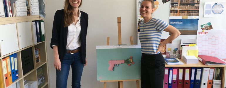 Christa Zahlbruckner (Sammlungsdigitalisierung) und Elisabeth Schlögl (Mitarbeiterin Museumsforum) stehen in einem Büro vor Ordnern und einer Staffelei.