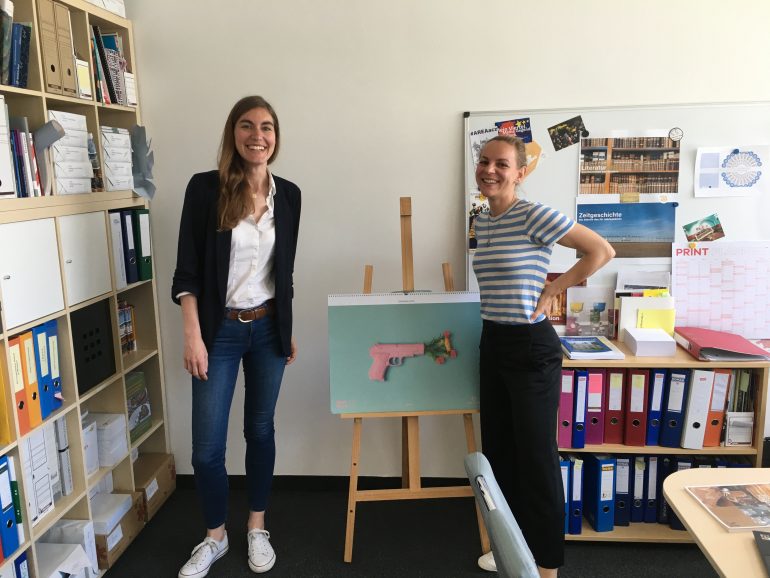 Christa Zahlbruckner (Sammlungsdigitalisierung) und Elisabeth Schlögl (Mitarbeiterin Museumsforum) stehen in einem Büro vor Ordnern und einer Staffelei.