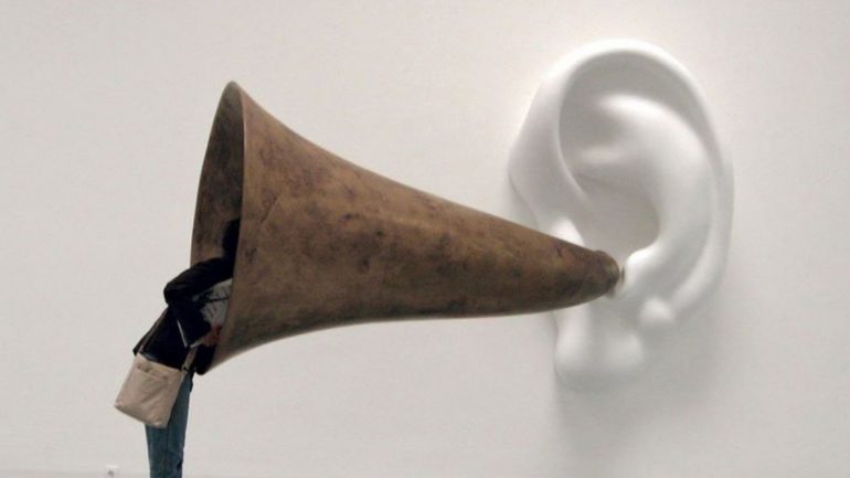 Abgebildet ist das Sujetbild des Workshops Museum als Soundscape der Museumsakademie: Eine Frau, die durch ein Megaphon auf ein Ohr blickt.