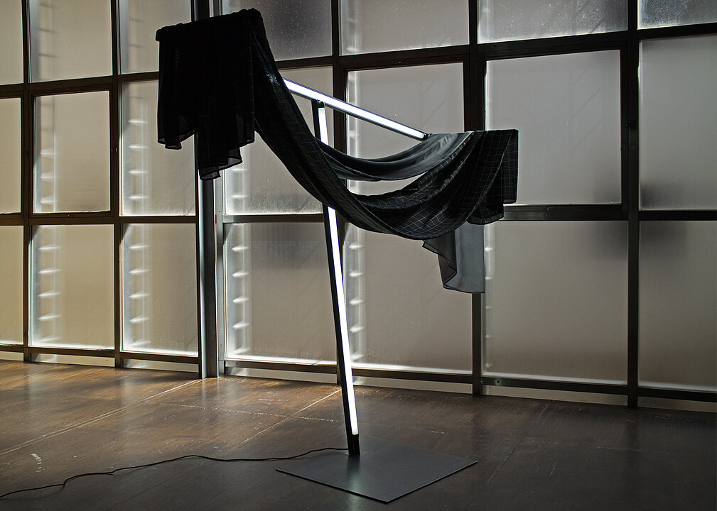 Kunstinstallation: in einem Raum hängen zwei schwarze Stofftücher über einem Gestell aus Leuchtstoffröhren.
