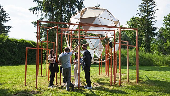 Jedes Jahr wird eine Schulklasse oder Studierengruppe um eine Adaptierung des Kunstwerks "In Then Out" der Klasse Tobias Rehberger 2014 angefragt. 2023 fügten Studierende der TU Graz dem Kunstwerk eine "Floating Oasis" hinzu. Es stellt eine architektonische Interpretation eines schwebenden Gewächshauses dar. 