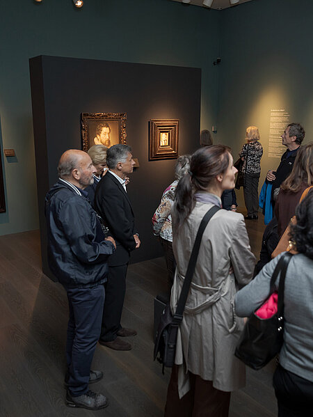 Eine Gruppe an Besucher:innen wird von einem Museumsmitarbeiter durch die Ausstellung "Zwischen Tanz und Tod" in der Alten Galerie geführt.