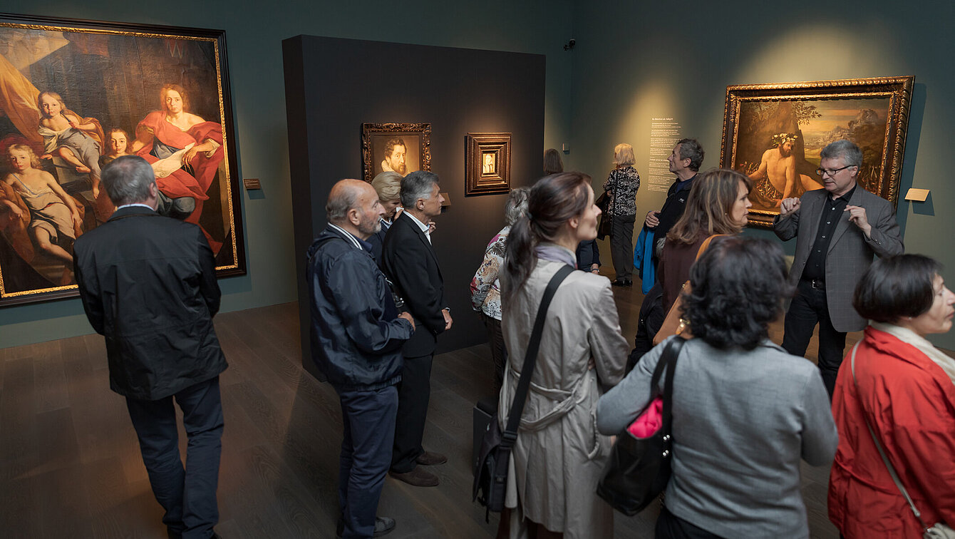 Eine Gruppe an Besucher:innen wird von einem Museumsmitarbeiter durch die Ausstellung "Zwischen Tanz und Tod" in der Alten Galerie geführt.