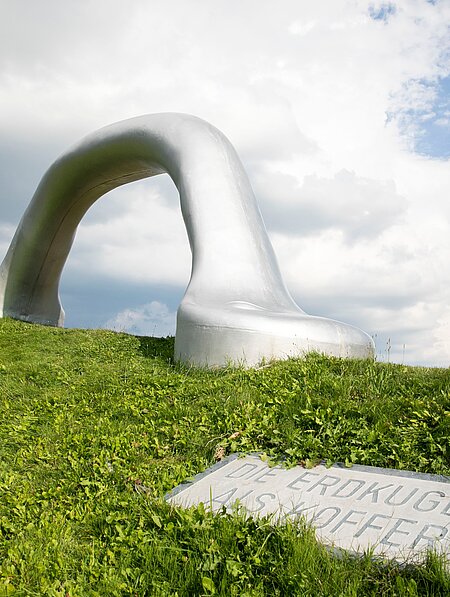 An oversized suitcase handle is positioned on the edge of one of the largest earth pyramids in the sculpture park. 