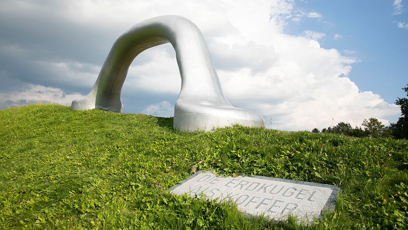 An oversized suitcase handle is positioned on the edge of one of the largest earth pyramids in the sculpture park. 