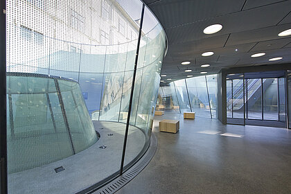 Das unterirdische Besucher*innen-Zentrum des Joanneumsviertels mit gläsernen Trichtern, die Blicke nach oben auf die Museumsgebäude.