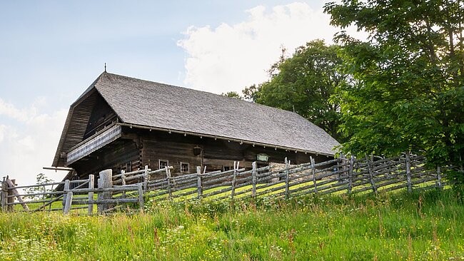 Hinter einem Bänderzaun das Geburtshaus Peter Roseggers