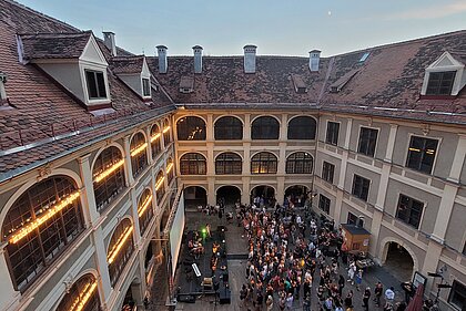 People stand in front of a stage in the Lesliehof in the Joanneumsviertel and listen to a concert.