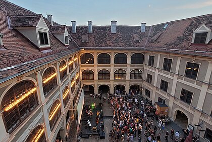 Menschen stehen vor einer Bühne im Lesliehof im Joanneumsviertel und hören einem Konzert zu.