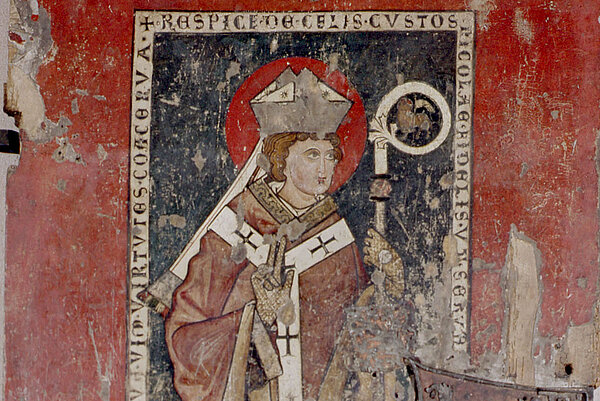 Mittelalterliche Wandmalerei eines Bischofs mit Mitra, Stab und Messgewand auf rotem Hintergrund; das Bild ist stark beschädigt und partiell abgerieben.