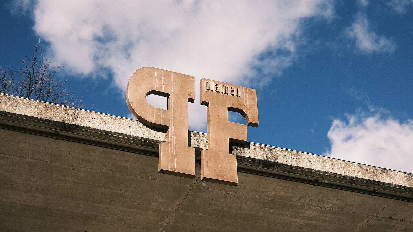 Large letters P and F with a lower case "plamen" at the top of the F. The letters are a reference to the lettering on the title page of an issue of the former Czechoslovakian magazine for literature, art and life plamen (German: Flamme) from 1965. At the same time, Plamen is the first name of the Austrian-Bulgarian artist.