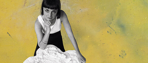 The artist Helen Chadwick is sitting next to one of her sculptures, titled “Piss Flowers,” and looking up out of the picture. The background shifts between green and yellow; the colored area is actually a photograph of dyed latex fabric.