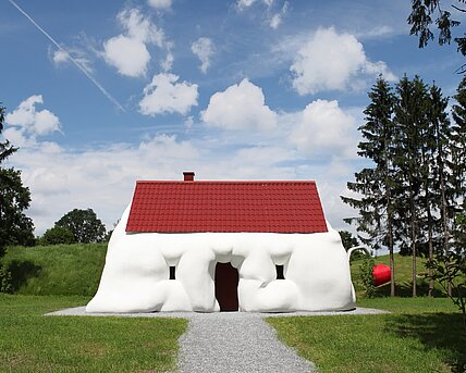 Ein aufgequollenes Einfamilienhaus thematisiert Reichtum und Konsum. 