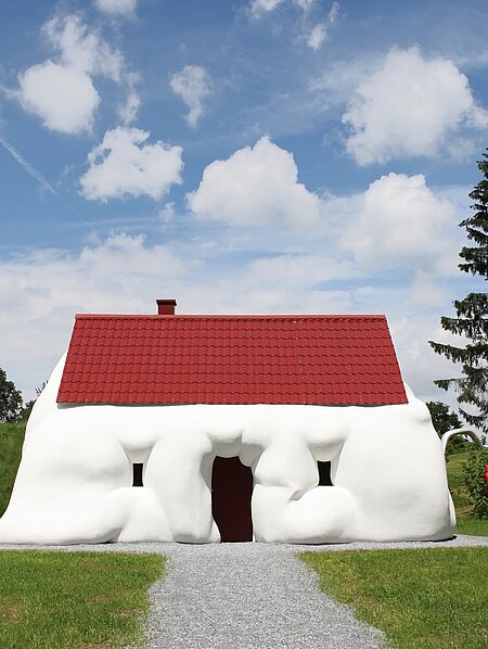 Ein aufgequollenes Einfamilienhaus thematisiert Reichtum und Konsum. 