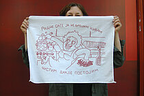 Eine Frau vor rotem Hintergrund hält ein besticktes Tuch vor ihr Gesicht, in dem eine Karikatur einer Frau in einer Küche zu sehen ist, die gleichzeitig kocht und putzt. Ergänzt wird dieses Bild durch einen kyrillischen Titel.