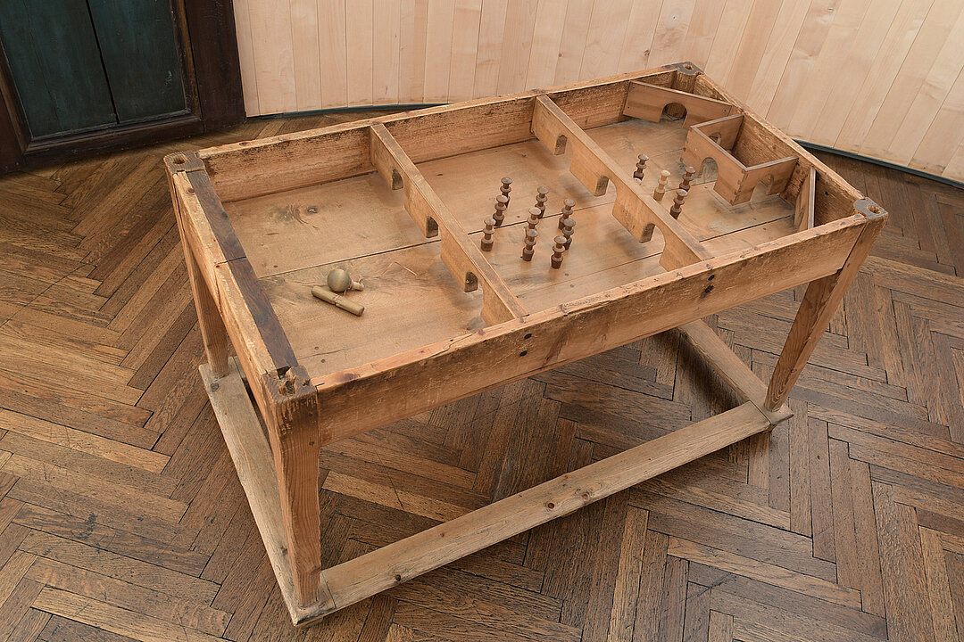 Brauner Tisch ohne Tischplatte. Anstelle der Tischplatte befindet sich ein eingebautes Spiel mit kleinen Kegel aus Holz.