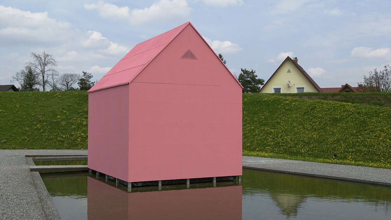 Am Seerosenteich neben dem Berggartencafé steht ein kleines rosa Einfamilienhaus. Über einen Steg zugänglich können drei Projektionen im Inneren begutachtet werden. 