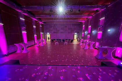 In the Heimatsaal in the Folk Life Museum there are high tables as well as lounge furniture. The hall is illuminated in magenta color.