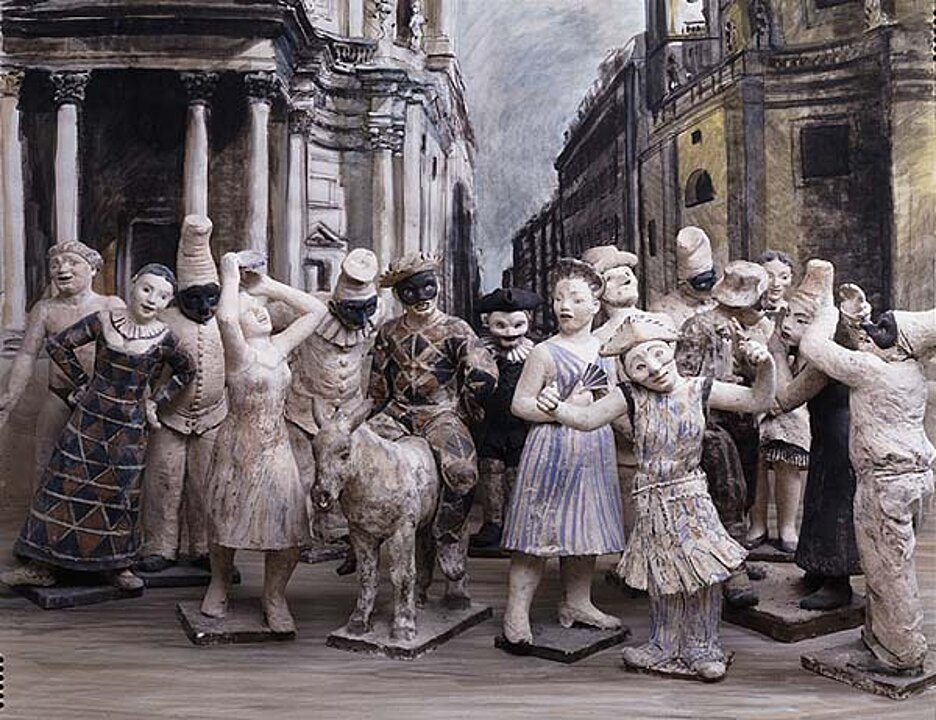 Foto von kleinen bleichen Figuren, die verschiedene Figuren des italienischen Volkstheaters zeigen. Viele Figuren tragen Masken. Ein reitet auf einem Esel.