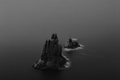ein schwarz-weoß Bild, welches eine dunkle Felslandschaft im Ozean zeigt.