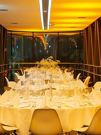 In the Needle in the Kunsthaus Graz, round gala tables are set up. The room is bathed in golden light, with matching table decorations on the tables.
