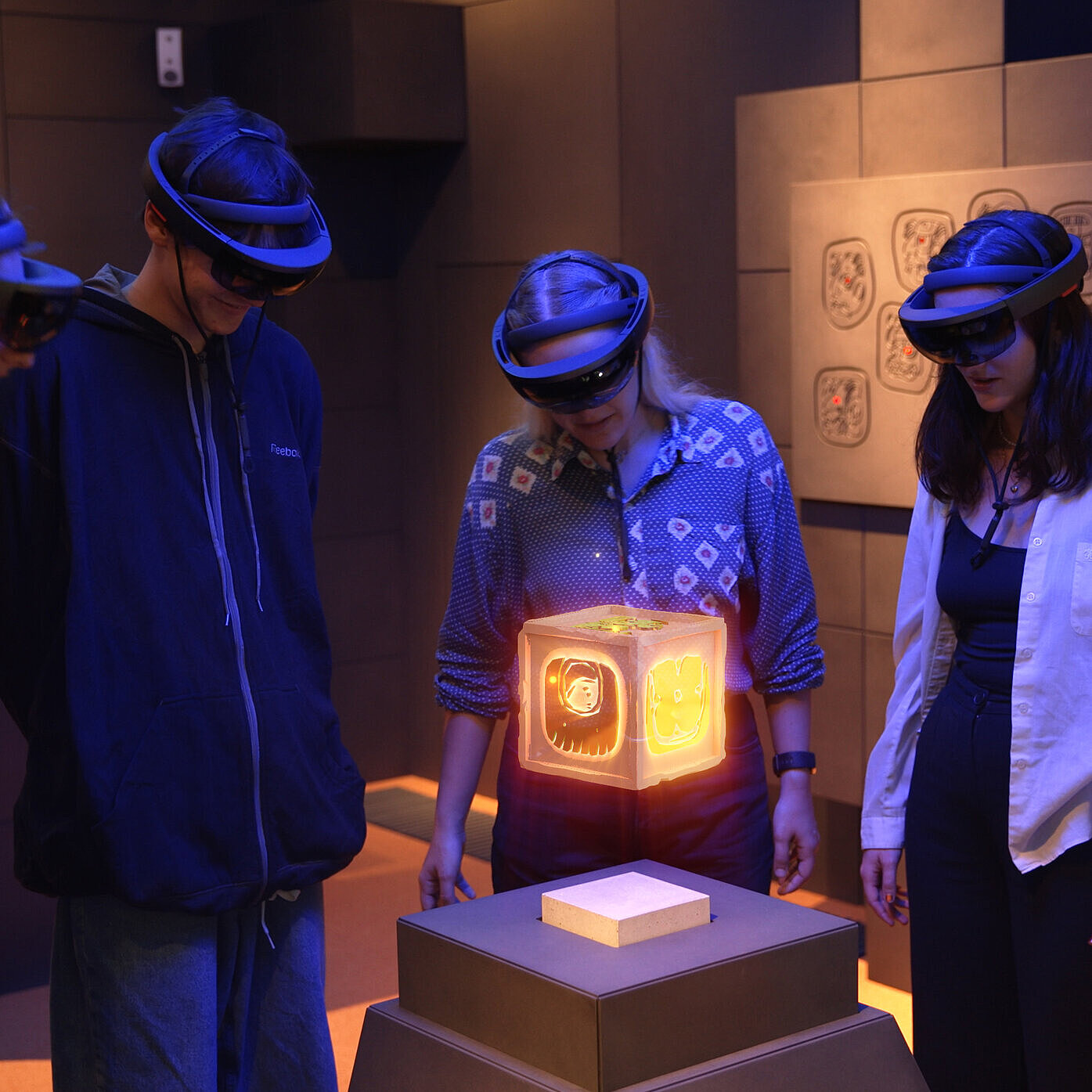 Eine Gruppe jugendlicher Besucher:innen mit AR-Brillen betrachtet eine virtuelle, leuchtende Box im AR-Raum des CoSAs.