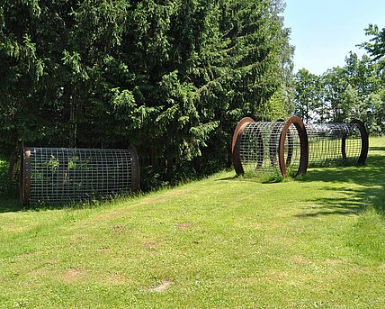 The three-part work consists of three open cylinders on a slope. Empty space can be experienced through the transparent grid structures, the hollow spaces of the cylinders themselves and the spaces between the objects.