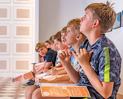 Kinder sitzen in einer Reihe und schauen an die Decke.