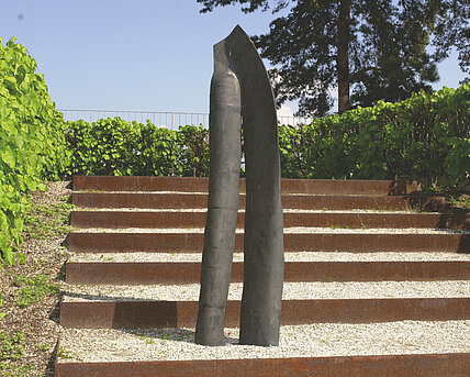 Metallskulptur aus zwei "Beinen", die am oberen Ende ineinander fließen. Die Künstlerin schafft eine abstrakte menschliche Skulptur durch das Weglassen aller Elemente, die für den erstrebten Ausdruck nicht unmittelbar von Bedeutung sind