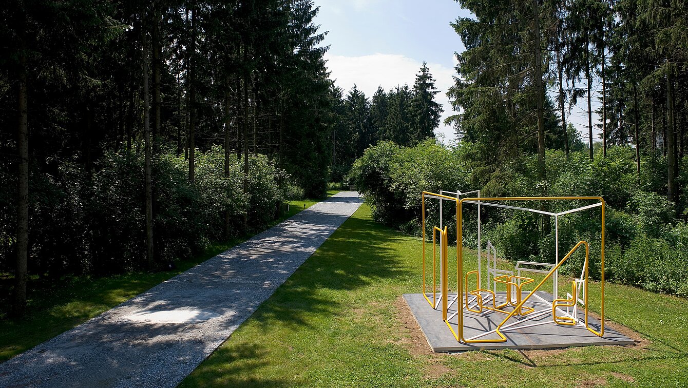 Ein Raum aus runden Metallrohren, in dem Wände und Gegenstände nur Umrissen sind. Die Schattenlinien werden durch eckige Stahlrohre ergänzt. Uncinis Werk steht im Berggarten des Skulpturenparks. 