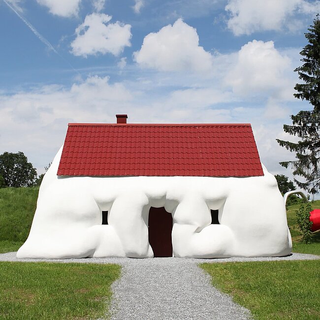 Ein aufgequollenes Einfamilienhaus thematisiert Reichtum und Konsum. 