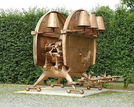 Die Skulptur ist übergroß, kupferfarben und steht auf einem flachen Sockel. Sie steht auf vier Füßen und hat mechanische und und biologische Elemente, die diesem Objekt etwas Lebendiges verleiht.  