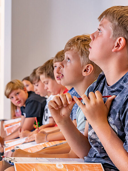 Kinder sitzen in einer Reihe und schauen an die Decke.