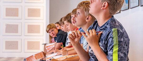 Kinder sitzen in einer Reihe und schauen an die Decke.