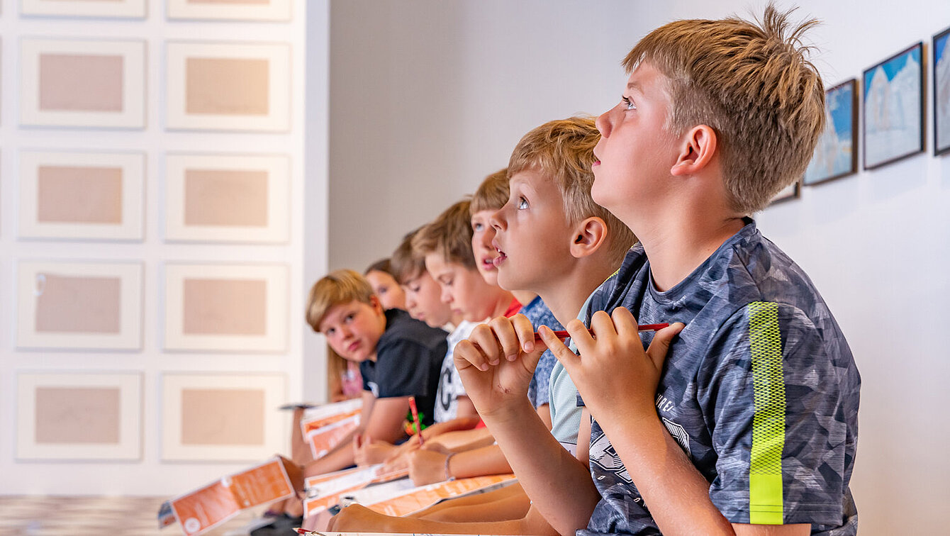 Kinder sitzen in einer Reihe und schauen an die Decke.