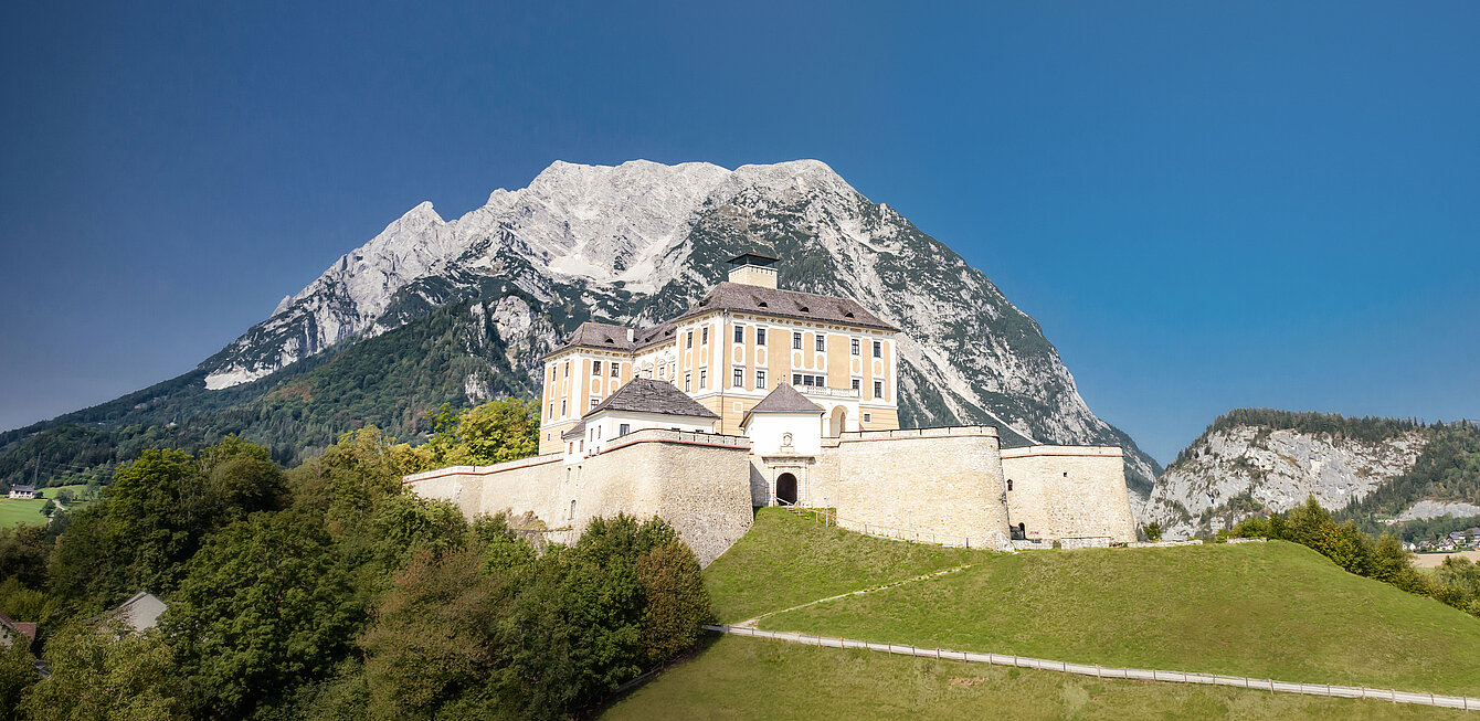 Ansicht auf Schloss Trautenfels bei blauem Himmel, im Hintergrund ist ein Berg zu sehen.