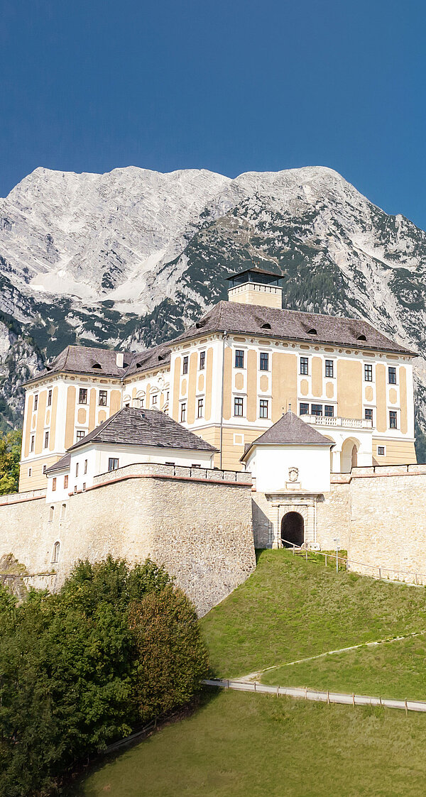 Ansicht auf Schloss Trautenfels bei blauem Himmel, im Hintergrund ist ein Berg zu sehen.