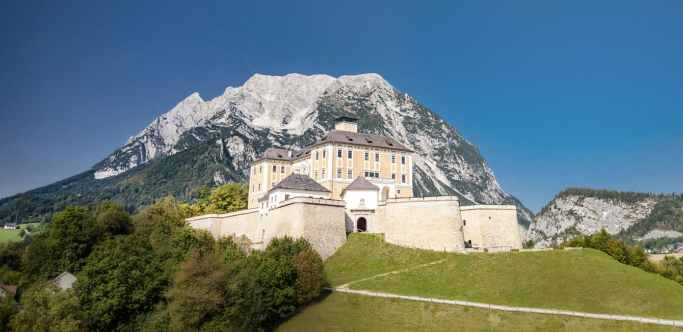 Ansicht auf Schloss Trautenfels bei blauem Himmel, im Hintergrund ist ein Berg zu sehen.