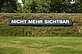 Weißer Schriftzug auf schwarzem Untergrund innen am Wall des Skulpturenparks mit der Aufschrift "nicht mehr sichtbar". Auf der anderen Seite des Walls auf dem Gelände des Schwarzl Freizeitzentrums befindet sich das Gegenstück mit der Aufschrift "noch nicht sichtbar".