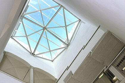 Weißes Treppenhaus mit modernen (Treppe und Geländer) und alten (Säulen) Elementen. 