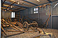 In a large showcase there are agricultural tools, e.g. a plow, a rake or a flail. There are stones on the floor.