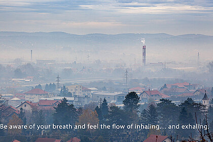 Ein Videostill eröffnet den Blick auf eine Vorstadt von industrieller Anmutung, über der schwerer Nebel liegt.