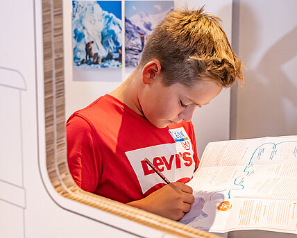 
A boy wearing a red T-shirt writes on a card