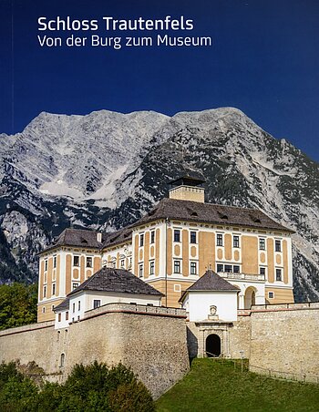 Buchcover des Katalogs Schloss Trautenfels. Auf dem Cover ist ein Foto von Schloss Trautenfels bei Sonne vor dem Berg Grimming abgedruckt