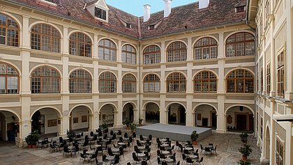 A large gray stage is set up in the Lesliehof in the Joanneumsviertel, along with coffeehouse seating.