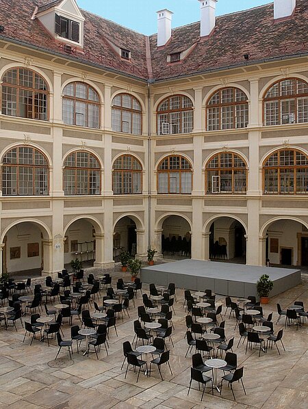 A large gray stage is set up in the Lesliehof in the Joanneumsviertel, along with coffeehouse seating.