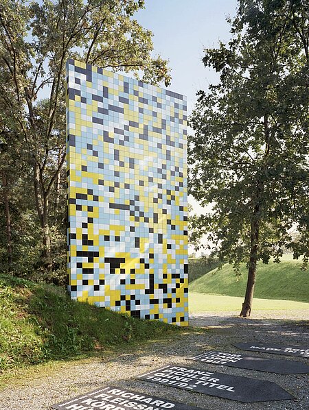 7 m high and 4 m wide, the sculpture grows out of a hill and thus appears to form a similar connection with the park as the surrounding trees. The scientific starting point for the sculpture is the completion of the Human Genome Project in 2001, in which the 3.2 billion base pairs of human DNA were decoded. Schlick replaces the four building blocks of the genome with cheaply produced tiles from Italy in four different colors.