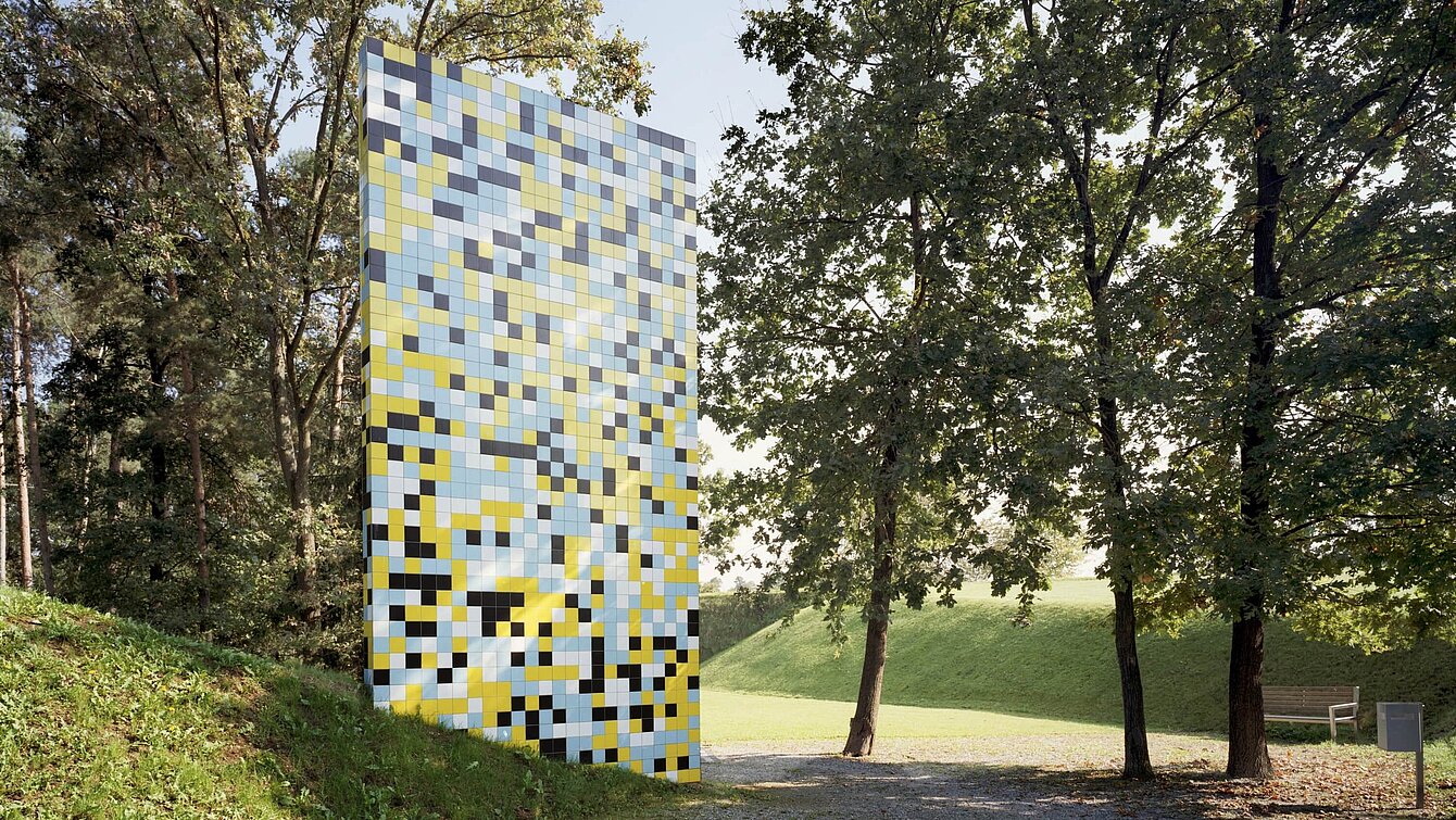 7 m high and 4 m wide, the sculpture grows out of a hill and thus appears to form a similar connection with the park as the surrounding trees. The scientific starting point for the sculpture is the completion of the Human Genome Project in 2001, in which the 3.2 billion base pairs of human DNA were decoded. Schlick replaces the four building blocks of the genome with cheaply produced tiles from Italy in four different colors.