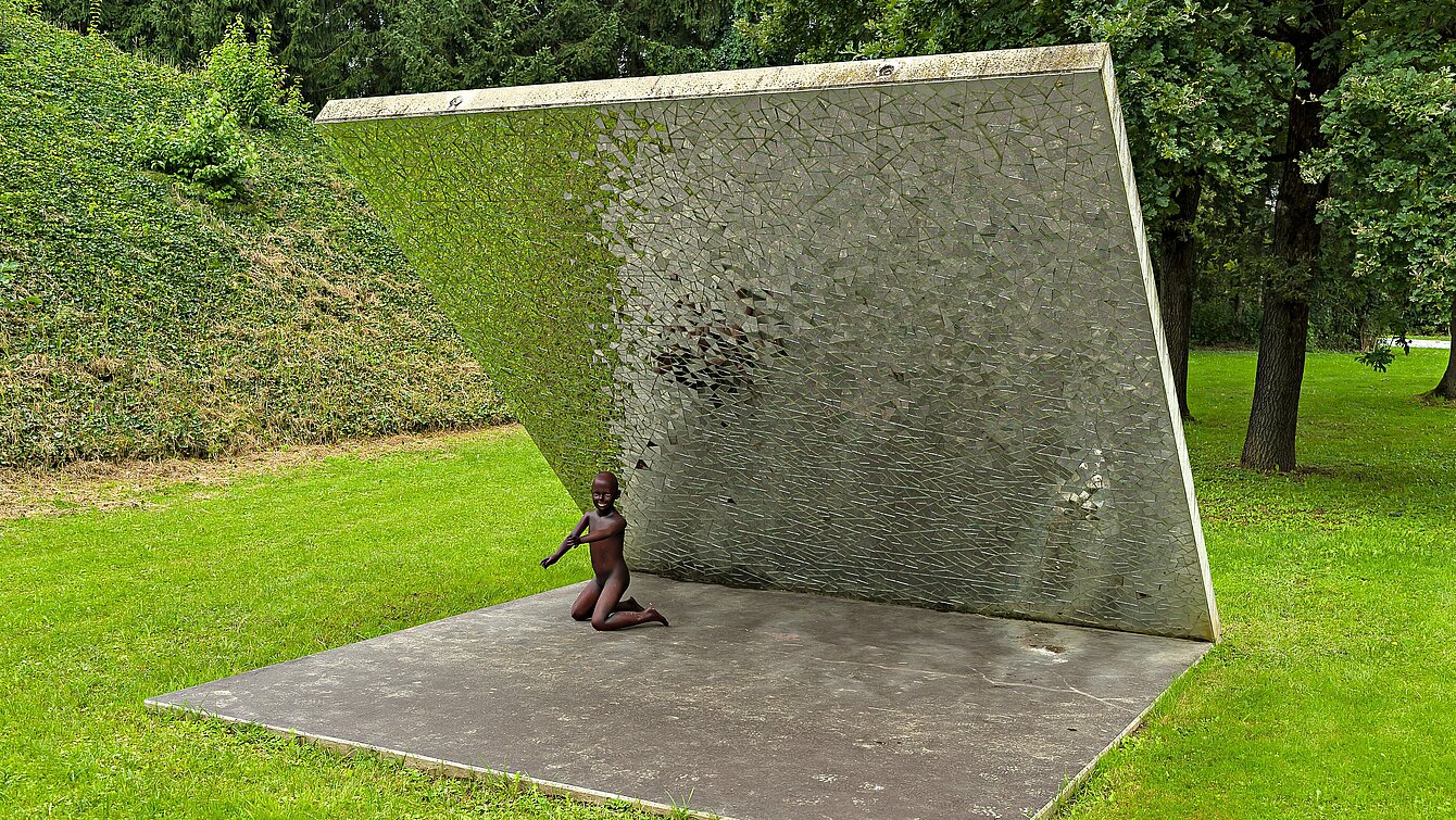 Im Berggarten des Skulpturenparks steht eine diagonal aufragende Betonwand. Sie ist unterseits mit kleinen Spiegelstücke versehen. Die Umwelt wird durch das Sonnenlicht in den Scherben gebrochen. 